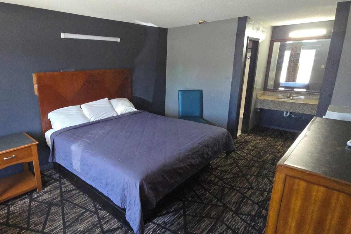 Ein Hotelzimmer mit einem großen Bett, einem Nachttisch aus Holz, einer Kommode und einem Badezimmer mit Spiegel und Waschbecken.