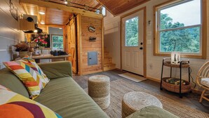 A cozy cabin interior with a wooden interior, a dining area, and a large window offering a view of the forest.