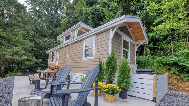 A small, two-story cabin with a deck, outdoor seating, and potted plants.