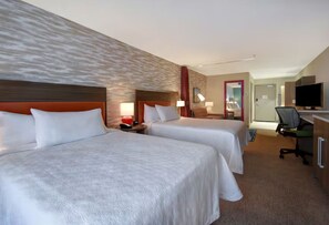 A hotel room with two beds, a desk, a chair, a television, and a bathroom visible through an open door.