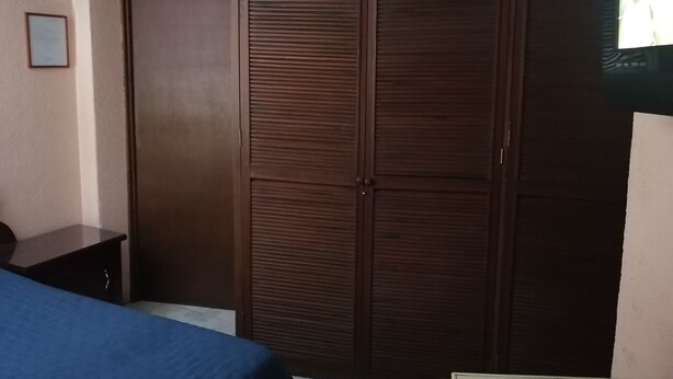 A bedroom with a large wardrobe, a bedside table, and a bed with a blue cover.