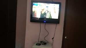 A television mounted on a wall above a small white cabinet with a power strip on top.