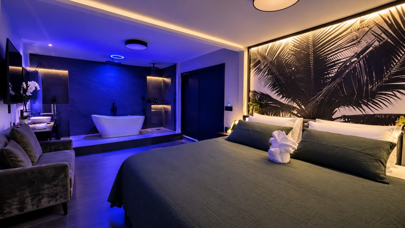 Un dormitorio moderno con una cama grande, una bañera y un televisor montado en la pared.