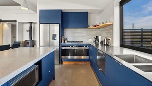 A modern kitchen with a central island, stainless steel appliances, and a large window offering a view. - Eight On Jackson - Luggate Holiday Home (Cromwell)