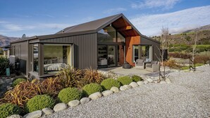 A modern house with a sloped roof, large glass windows, and a patio area with outdoor furniture. - Eight On Jackson - Luggate Holiday Home (Cromwell)