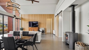 A modern living room with a dining area, a TV, and a wood-burning stove. - Eight On Jackson - Luggate Holiday Home (Cromwell)