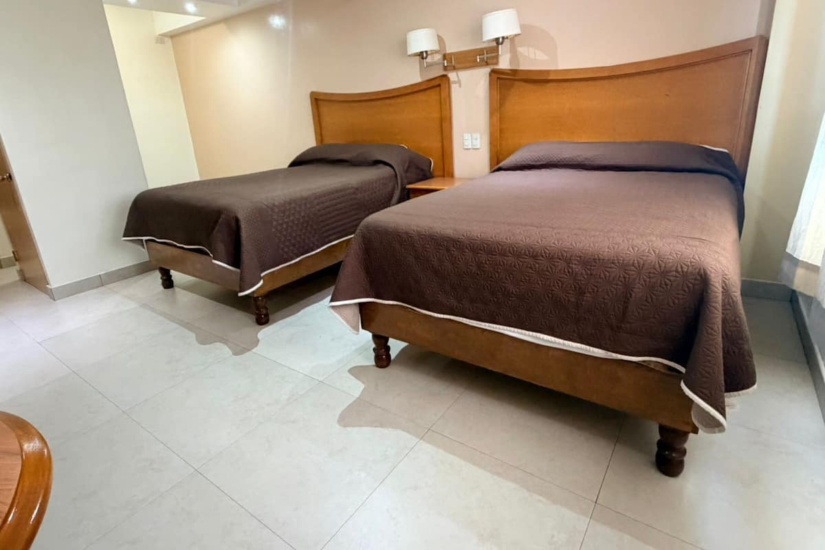 Una habitación de hotel con dos camas, cabecero de madera, mesita de noche y lámparas de pared.