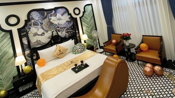 A hotel room with a large bed, a seating area with two chairs, a small table, and a decorative wall.
