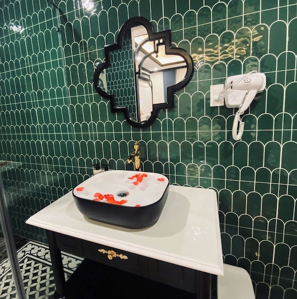 A bathroom with a white sink, green tiled walls, a gold faucet, and a white telephone.