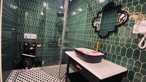 A bathroom with green tiled walls, a black and white patterned floor, a sink with a black basin, and a shower area.