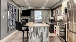 A modern kitchen with a central island, stainless steel appliances, and a large window. - Modern 2BR Condo with secure parking and walking distance to Rogers Place  (Edmonton)