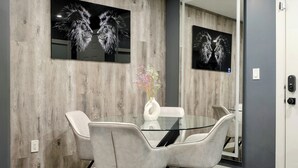 A modern dining area with a glass table, white chairs, and a vase with flowers. - Modern 2BR Condo with secure parking and walking distance to Rogers Place  (Edmonton)