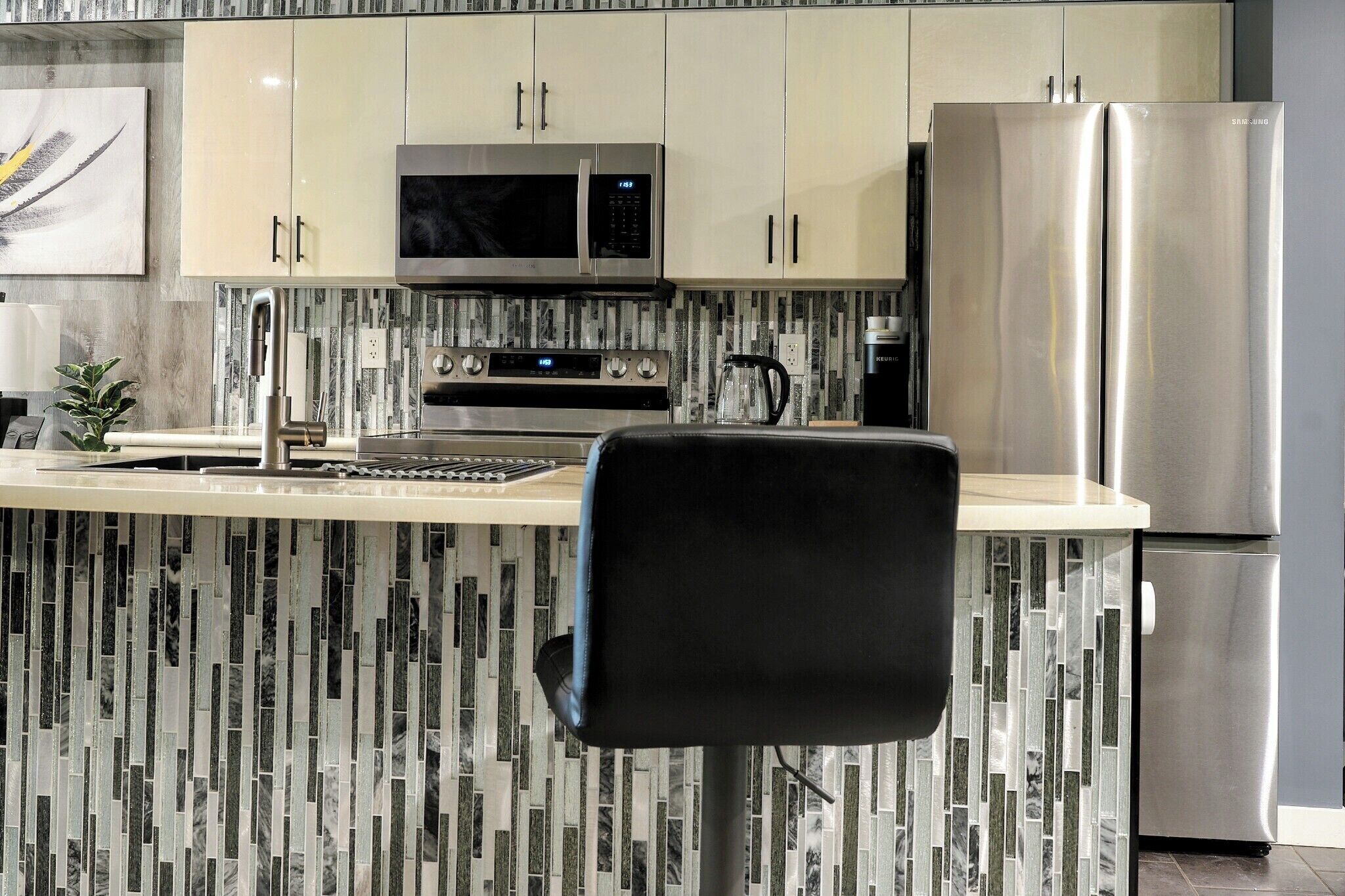 Cozinha com ilha central, eletrodomésticos de aço inoxidável e painel de azulejos.