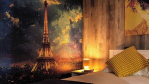 A bedroom with a large mural of the Eiffel Tower, a wooden headboard, a bedside table with a lamp, and a yellow textured pillow. - Modern 2BR Condo with secure parking and walking distance to Rogers Place  (Edmonton)