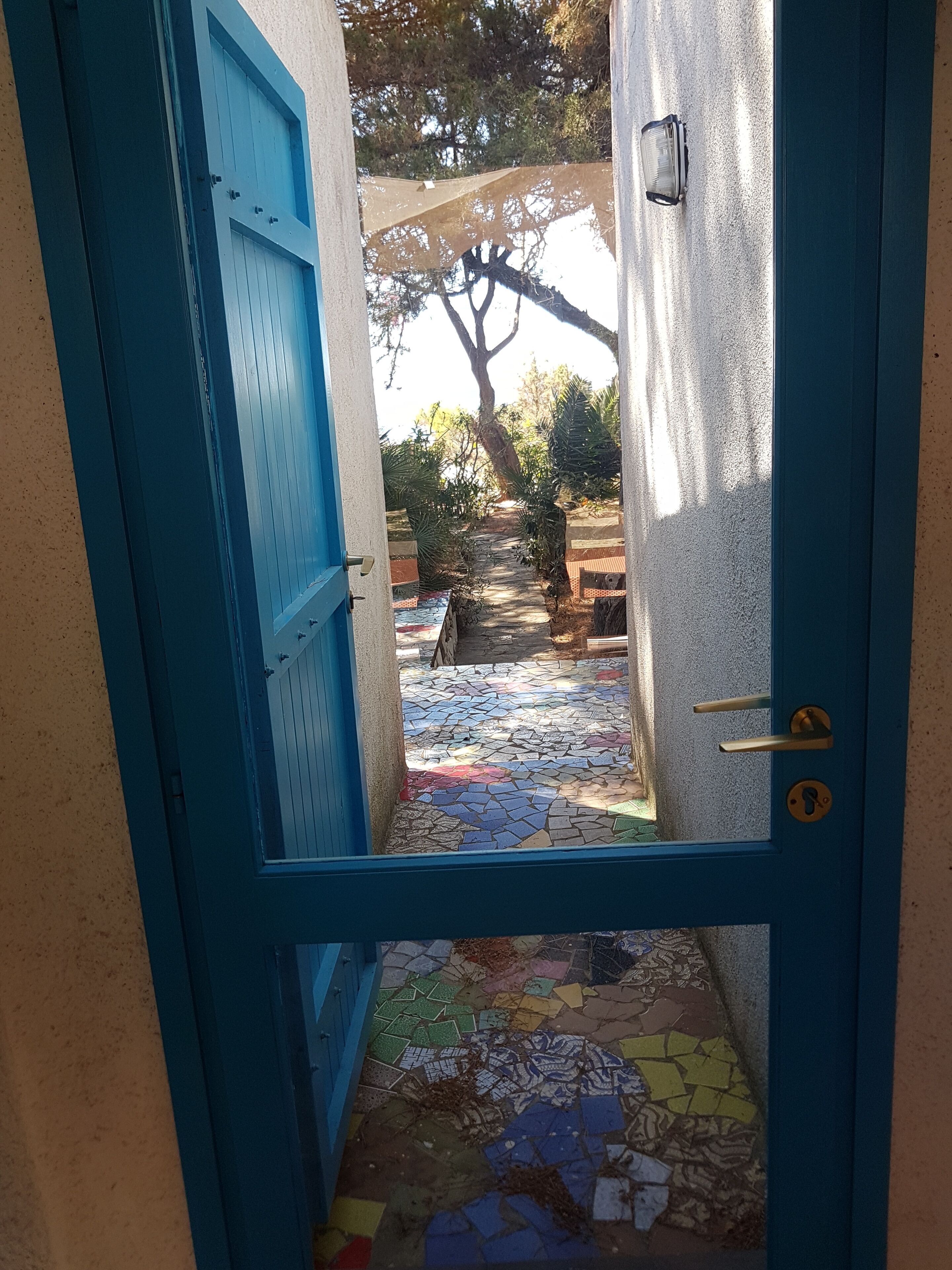 Eine blaue Tür führt zu einer gefliesten Terrasse mit Baum und Gartenmöbeln.