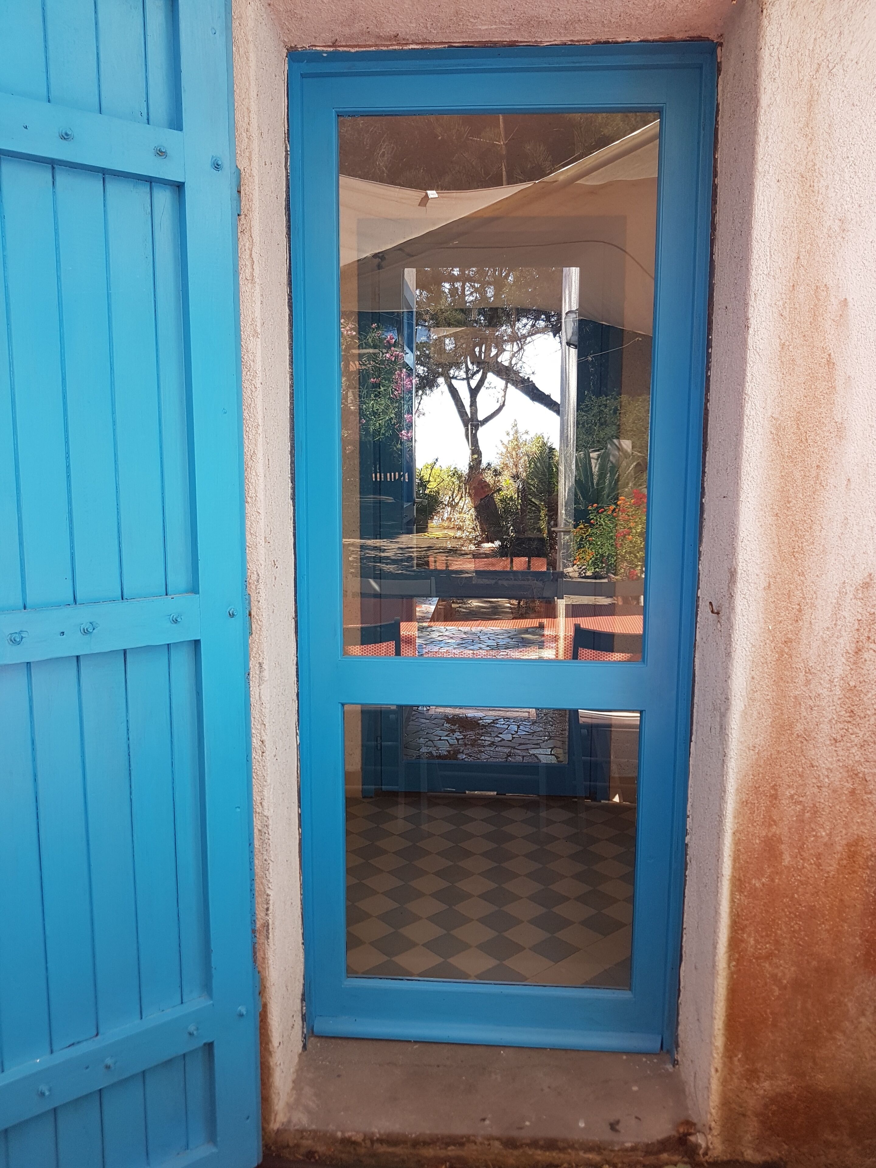 Ein blau gerahmtes Fenster mit Blick auf eine Außenpatio-Terrasse, einschließlich eines Baumes und Blumentöpfen.