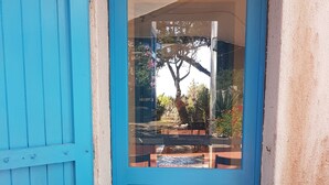 A blue-framed window with a view of an outdoor patio area, including a tree and potted plants. - Beachfront villa, right ON SAND! (Cala Liberotto)