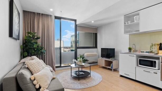 Una sala de estar moderna con sofá, una mesa de centro, televisor y una zona de cocina con microondas.
