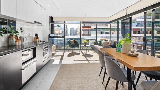 A modern kitchen with a dining area, large windows, and a view of the cityscape.