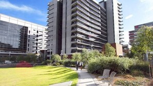 A modern high-rise building with multiple balconies, surrounded by a well-maintained lawn and pathway.