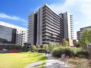 A modern high-rise building with multiple balconies, surrounded by a well-maintained lawn and pathway.