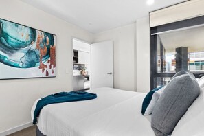 A hotel room with a bed, a painting, a window, and a view of the city.