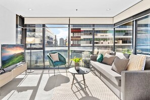 A modern living room with a sofa, armchair, TV, and a small table with a plant.