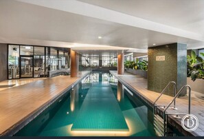 Una piscina con pavimento piastrellato, circondata da un pontile in legno e pareti in vetro.