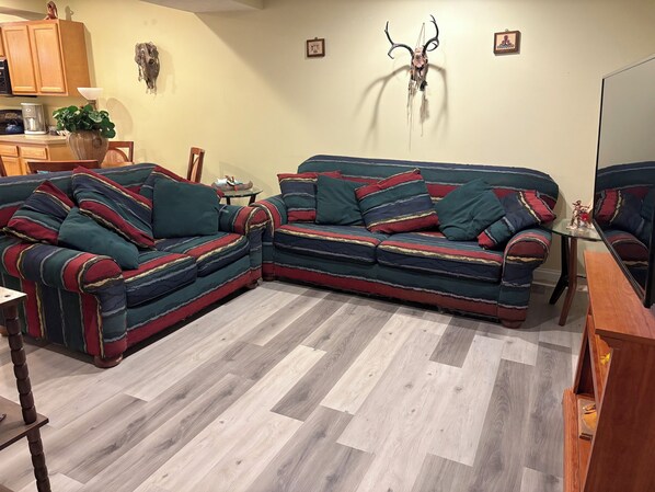 A living room with a sectional sofa, wooden flooring, and a wall-mounted deer skull decoration. - #10 Apartment with southwestern vibes. (Lorain)
