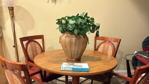 A dining area with a round wooden table, six wooden chairs with red cushions, a decorative vase with green foliage, and a book on the table. - #10 Apartment with southwestern vibes. (Lorain)