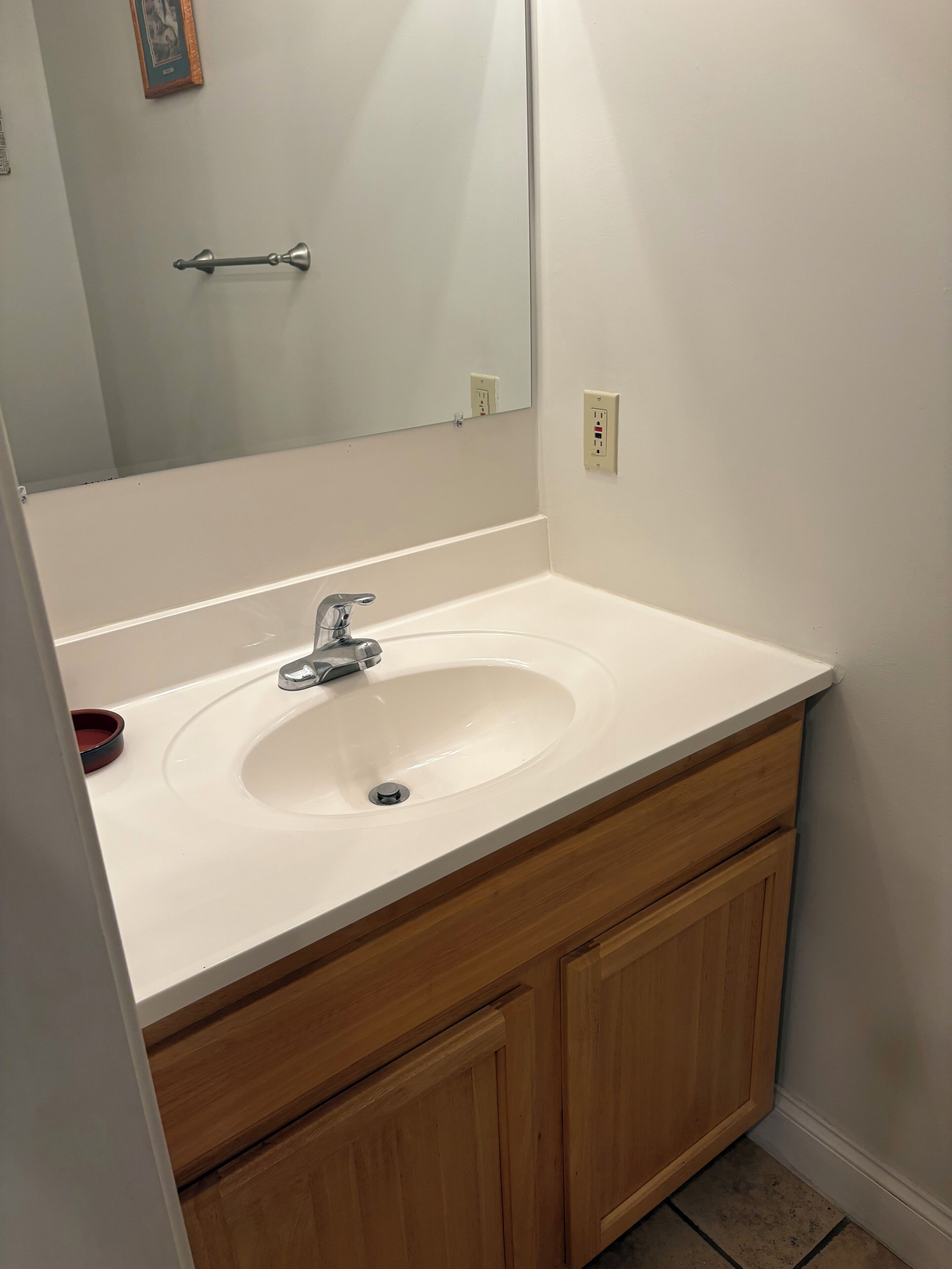 Un baño con lavamanos blanco, tocador de madera y un espejo.