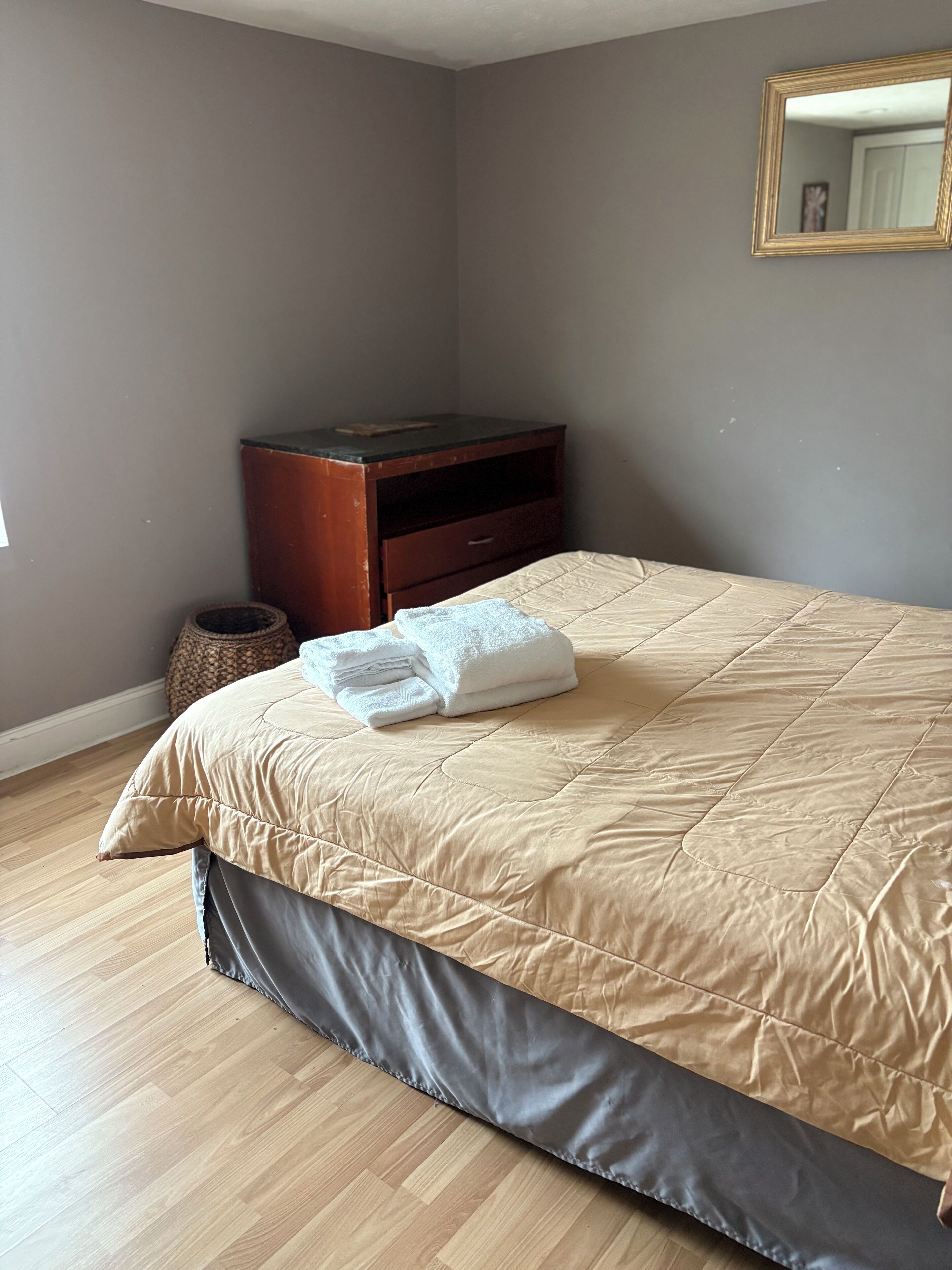 Un dormitorio con una cama, una mesita de noche de madera, un cubo de basura pequeño y un espejo en la pared.