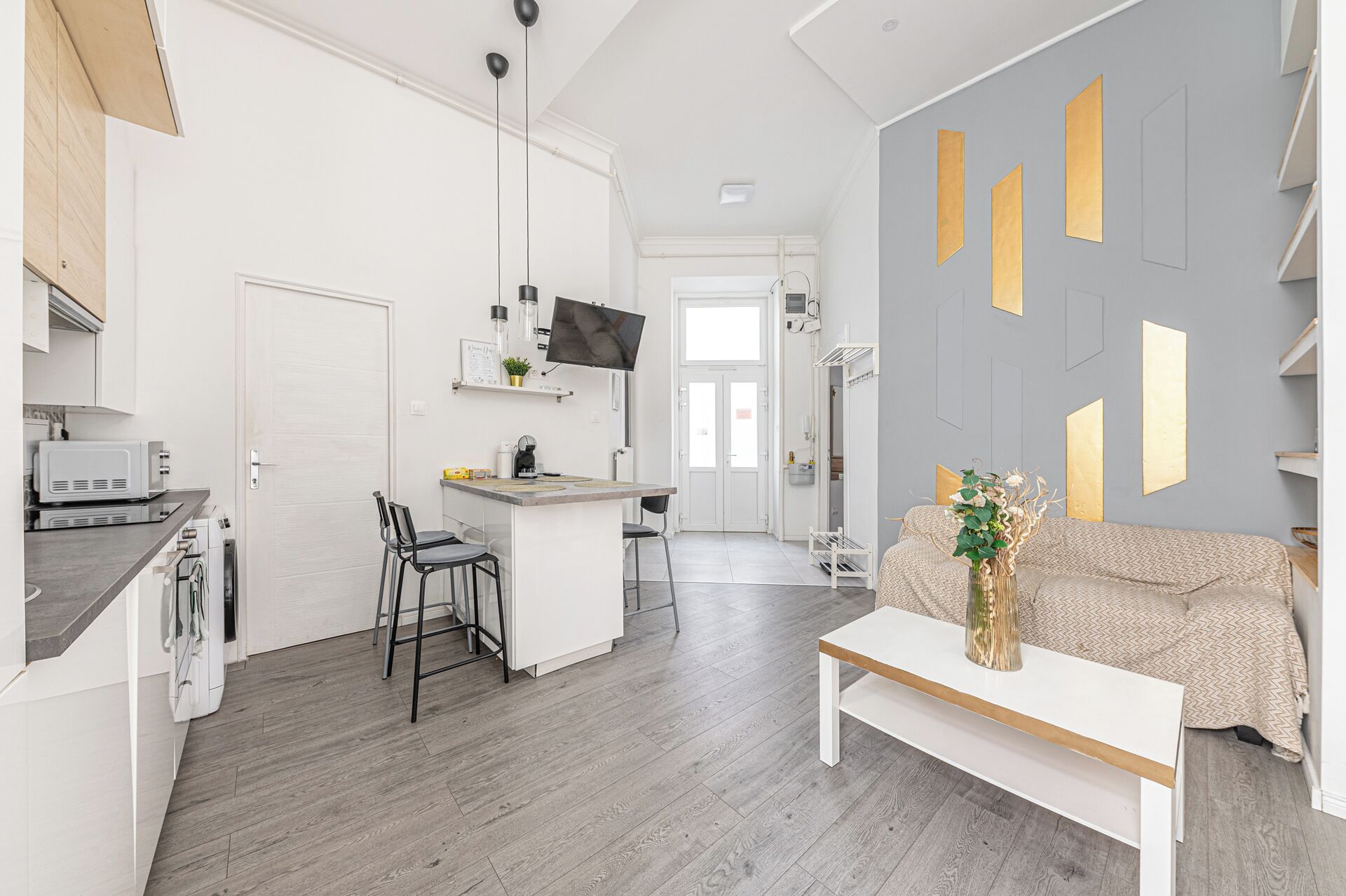 A modern kitchen with a dining area, a sofa, and a TV mounted on the wall.