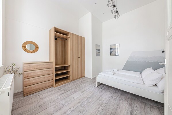 A bedroom with a bed, a wooden wardrobe, a mirror, and a picture on the wall.