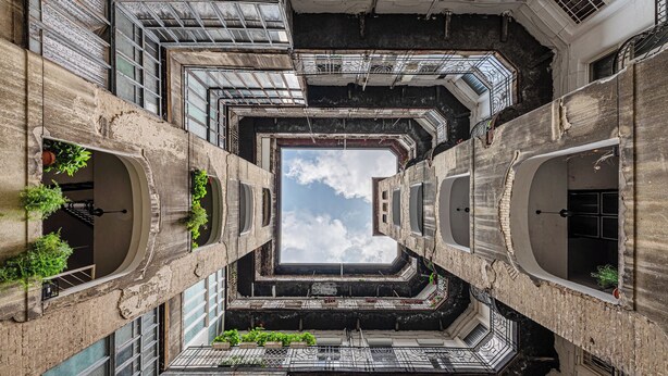 Un atrium à plusieurs niveaux, surmonté d’une verrière centrale et entouré de balcons ornés de plantes en pot.