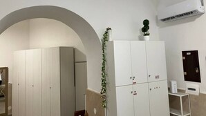 A room with a large arched doorway, a white wardrobe with multiple doors, a small potted plant on top, and an air conditioning unit mounted on the wall.