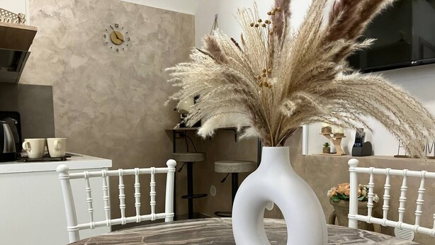 A dining table with a white vase and pampas grass, surrounded by white chairs in a modern kitchen setting.