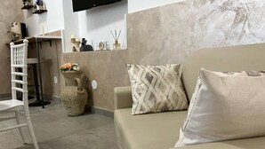 A modern living room with a beige sofa, a white chair, a decorative vase, and a wall-mounted TV.