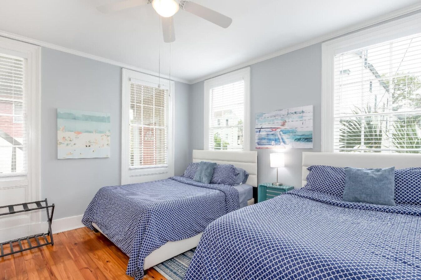 A bedroom with two beds, a ceiling fan, and large windows with blinds.