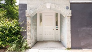 Une porte blanche surmontée d’un arc en briques, une boîte aux lettres et une plaque portant le numéro « 63 ».