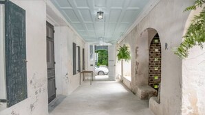 Un couloir avec un plafond blanc, une table et une voiture visible à travers une porte ouverte.