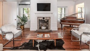 Un salon avec une cheminée, un téléviseur, un piano à queue et deux fauteuils blancs.