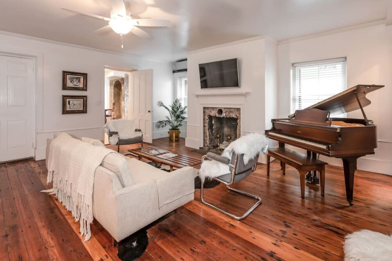 Ein Wohnzimmer mit Klavier, einer Couch, einem Sessel, einem Kamin und einem Fernseher.