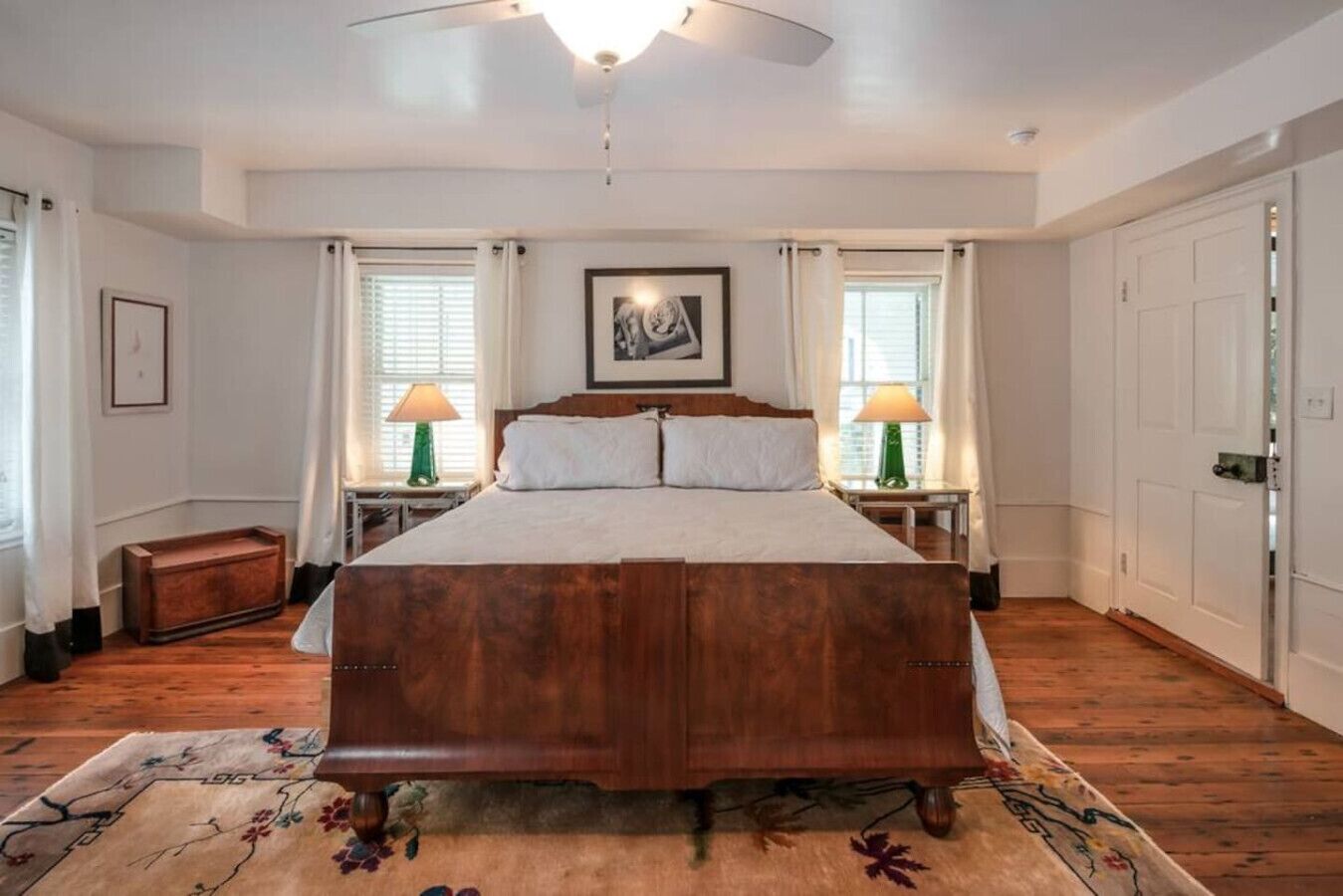A bedroom with a large bed, two bedside tables with lamps, a wooden bench, and a ceiling fan.