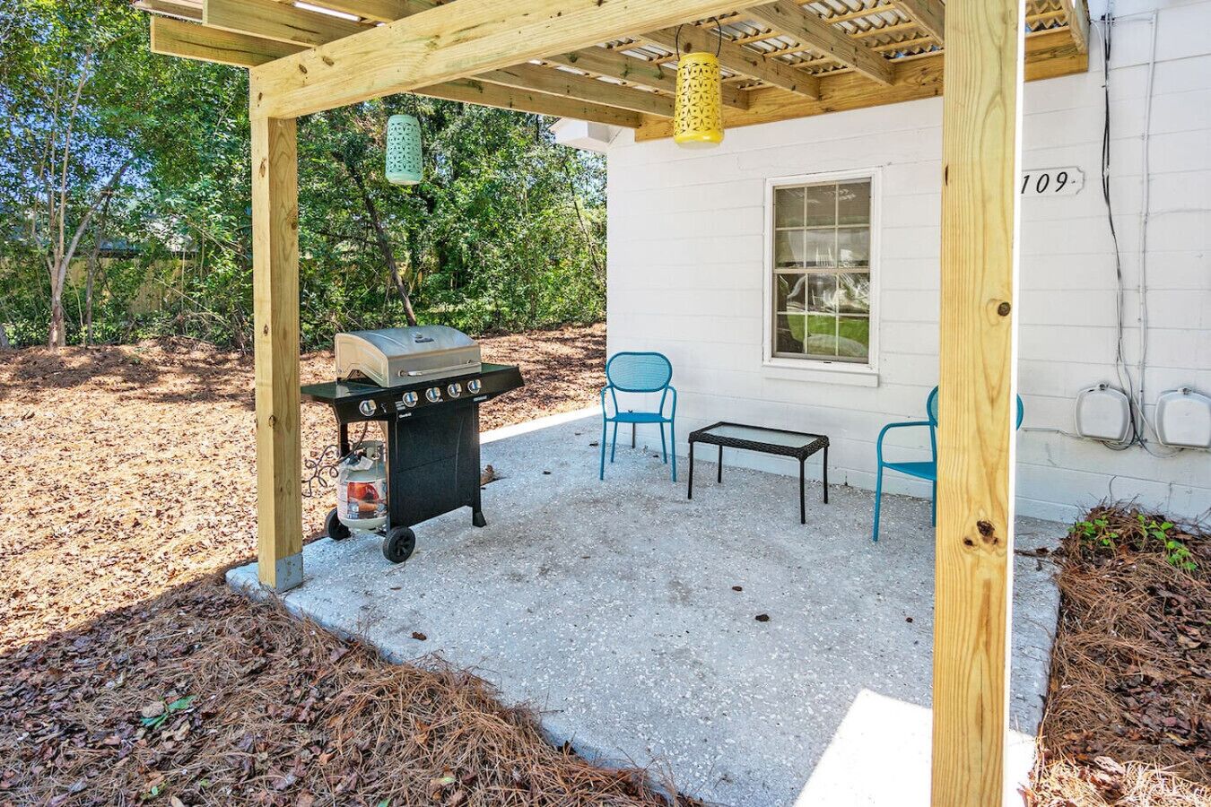 A covered patio with a grill, two chairs, a table, and a wooden post with a number.