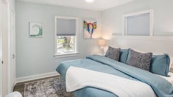 A bedroom with a bed, two windows with blinds, a ceiling fan, a rug, and a wall art piece.