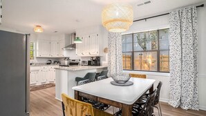 Una cocina moderna con armarios blancos, una mesa de comedor con sillas y un amplio ventanal con cortinas.