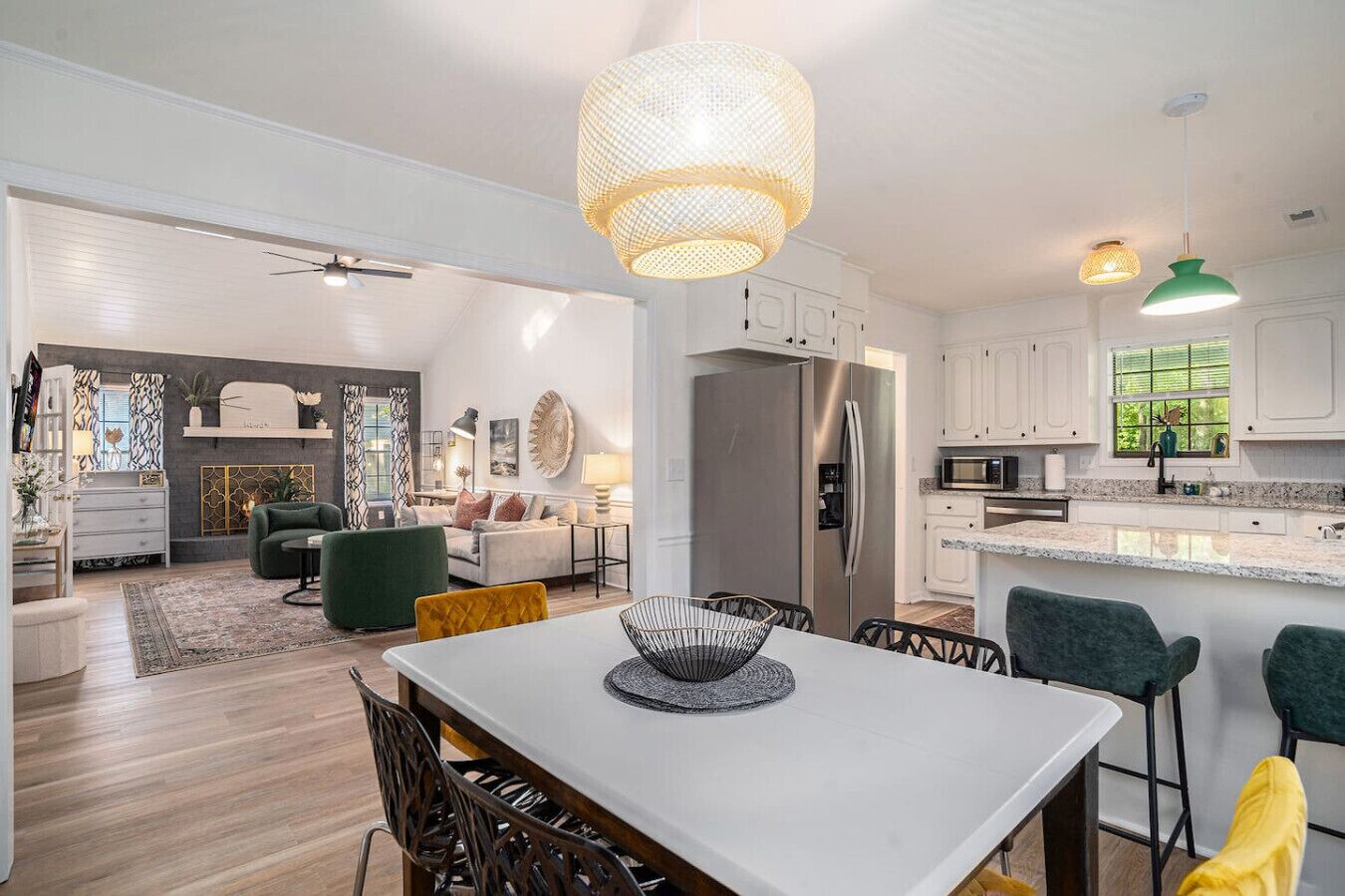 A modern kitchen with white cabinets, a stainless steel refrigerator, and a dining area with a white table and chairs.