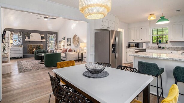 Una cocina moderna con armarios blancos, un refrigerador de acero inoxidable y un comedor con mesa y sillas blancas.