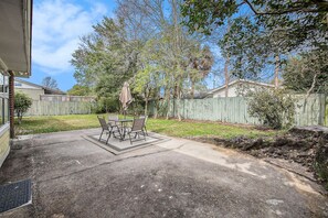A backyard patio with a table and chairs, surrounded by a wooden fence and trees. - Waylyn Chic~Very Convenient Location, Pool Table! (North Charleston)